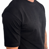 A man wearing a plain black short-sleeve crewneck t-shirt, shown from a side profile against a white background.