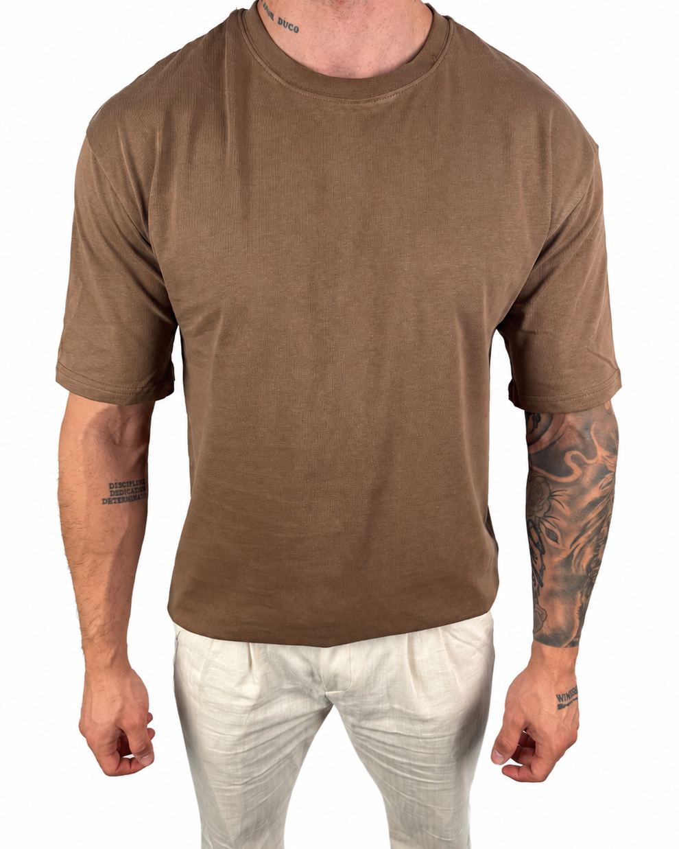 A man wearing a brown short-sleeve crewneck t-shirt and off-white pants, shown from the neck down against a plain white background.