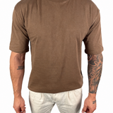 A man wearing a brown short-sleeve crewneck t-shirt and off-white pants, shown from the neck down against a plain white background.