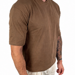 A man wearing a brown short-sleeve crewneck t-shirt and light beige linen pants, shown from the neck down against a solid white background.