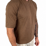 A man wearing a brown short-sleeve crewneck t-shirt and light beige linen pants, shown from the neck down against a solid white background.