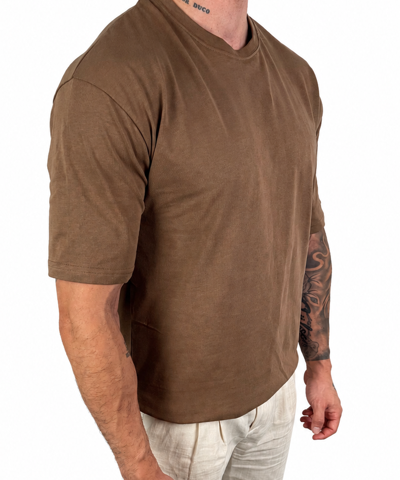 A man wearing a brown short-sleeve crewneck t-shirt and light beige linen pants, shown from the neck down against a solid white background.