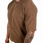 A man wearing a brown short-sleeve crewneck t-shirt and off-white pants, shown from the side against a plain white background.
