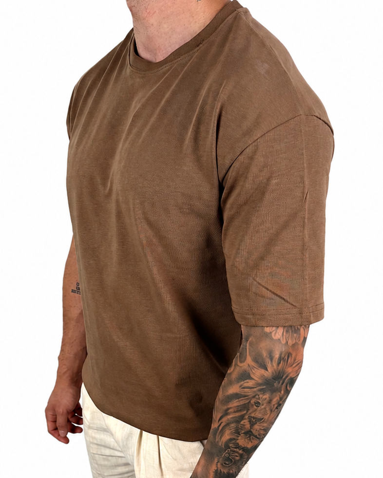 A man wearing a brown short-sleeve crewneck t-shirt and off-white pants, shown from the side against a plain white background.
