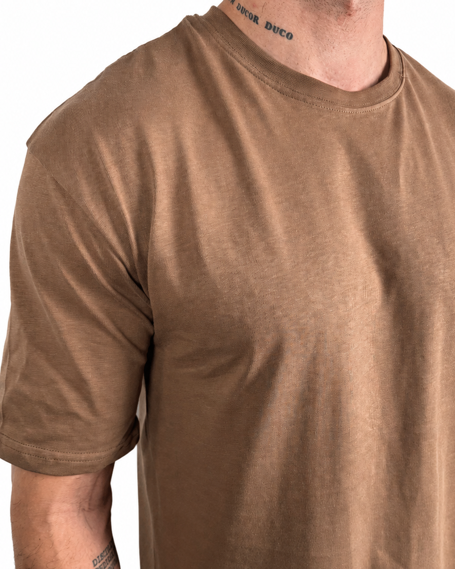 A man wearing a short-sleeve crewneck t-shirt in a washed, faded brown or tan color, shown from the neck down against a plain white background.