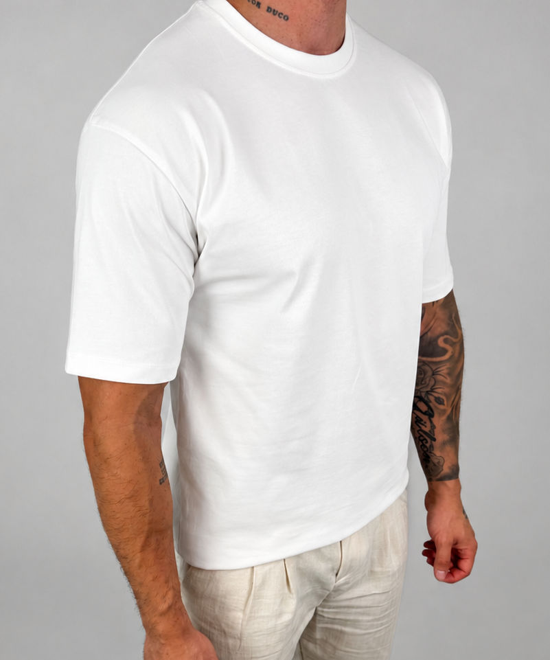 A man wearing a plain white short-sleeve crewneck t-shirt and light beige linen pants, standing against a neutral gray studio background.
