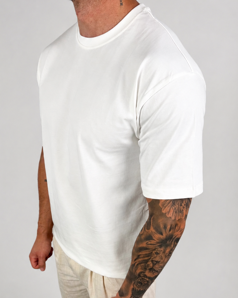 A man wearing a plain white short-sleeve crewneck t-shirt and light beige linen pants, standing against a light gray studio background.