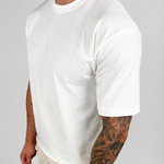 A man wearing a plain white short-sleeve crewneck t-shirt and light beige linen pants, standing against a light gray studio background.