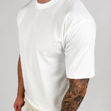A man wearing a plain white short-sleeve crewneck t-shirt and light beige linen pants, standing against a light gray studio background.
