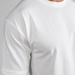 A man wearing a plain white short-sleeve crewneck t-shirt, paired with light beige trousers, shown from the neck down against a neutral gray background.
