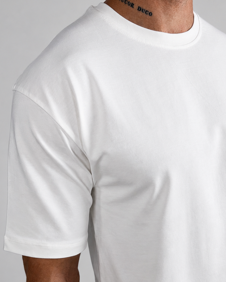 A man wearing a plain white short-sleeve crewneck t-shirt, paired with light beige trousers, shown from the neck down against a neutral gray background.