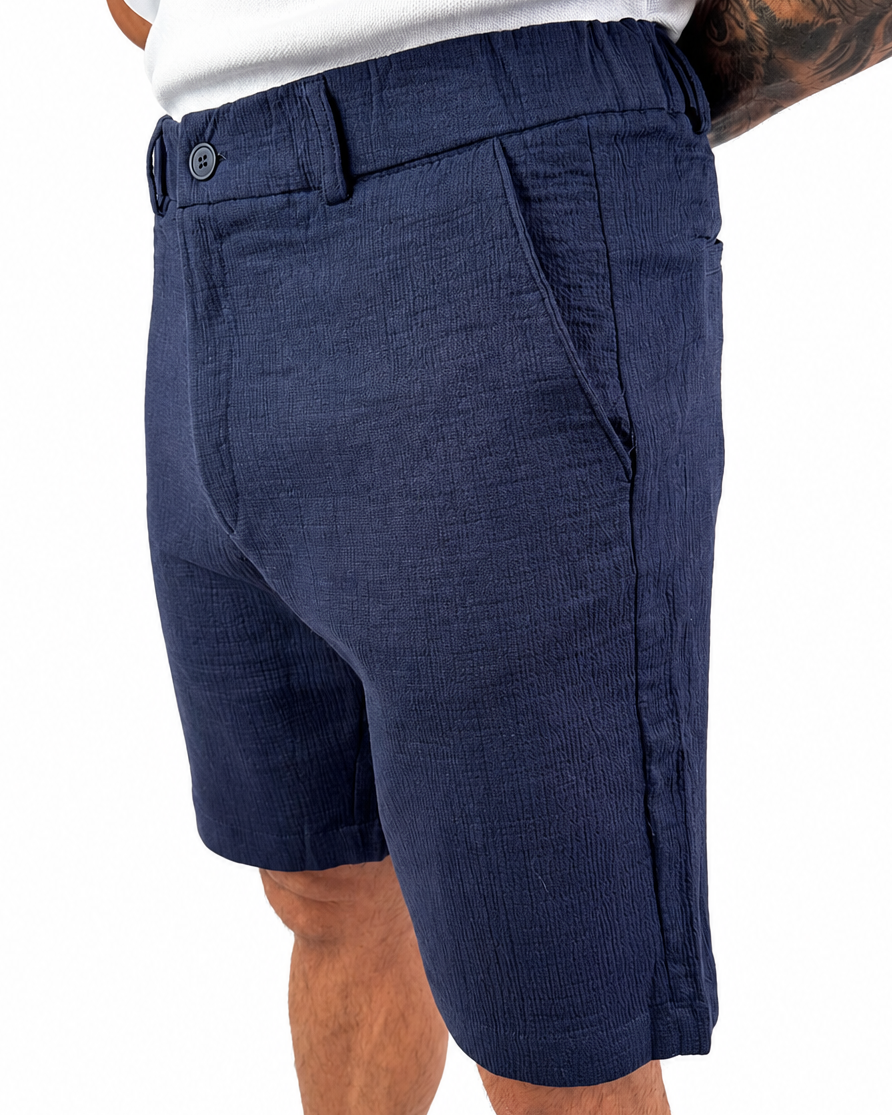 A man wearing navy blue textured shorts and a white t-shirt, shown from the waist down against a plain white background.