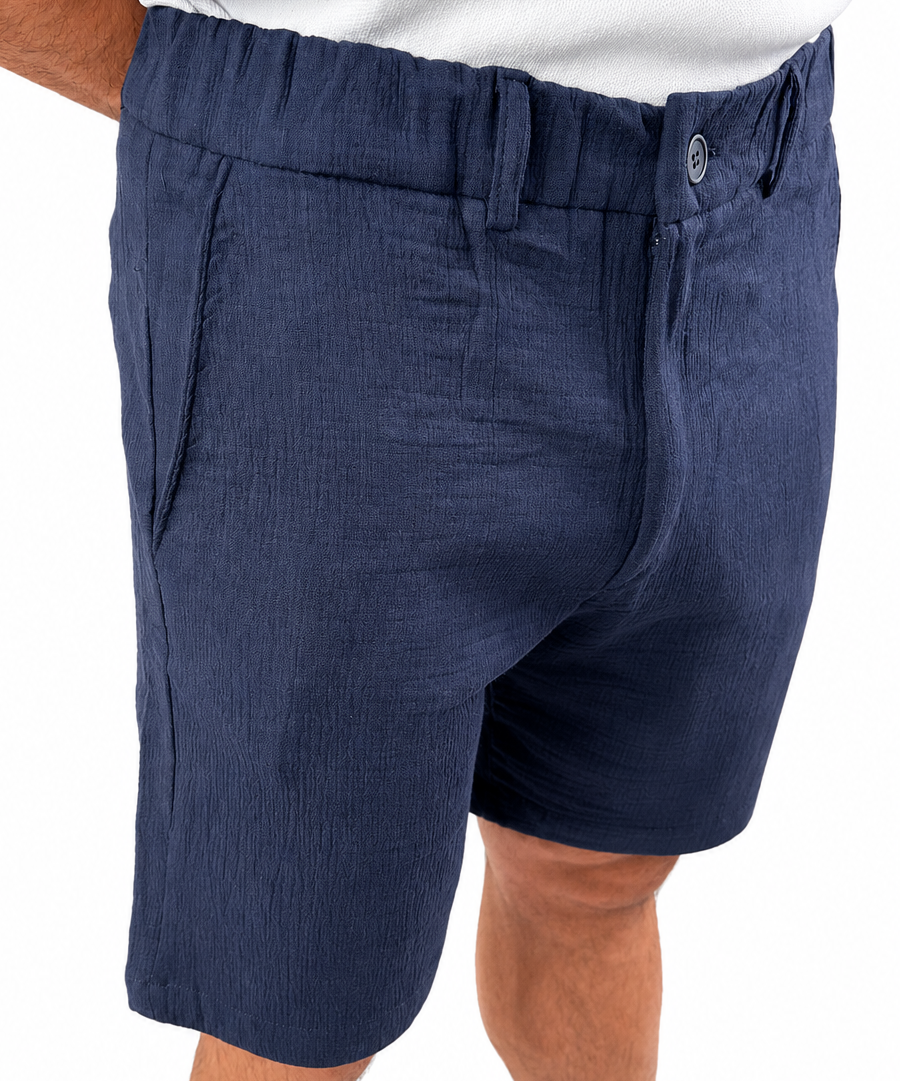 A close-up of a person wearing navy blue textured shorts with a white shirt partially visible at the top, against a plain white background.