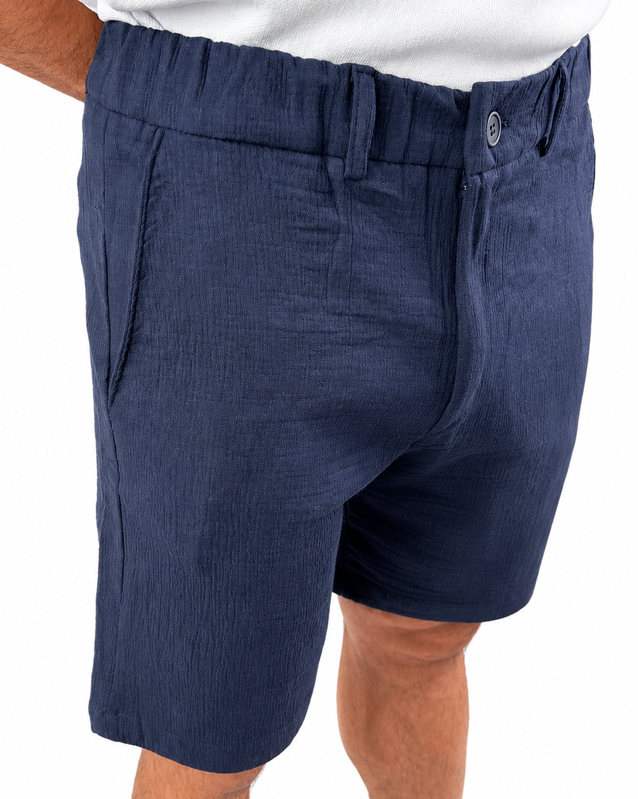 A close-up of a person wearing navy blue textured shorts with a white shirt partially visible at the top, against a plain white background.
