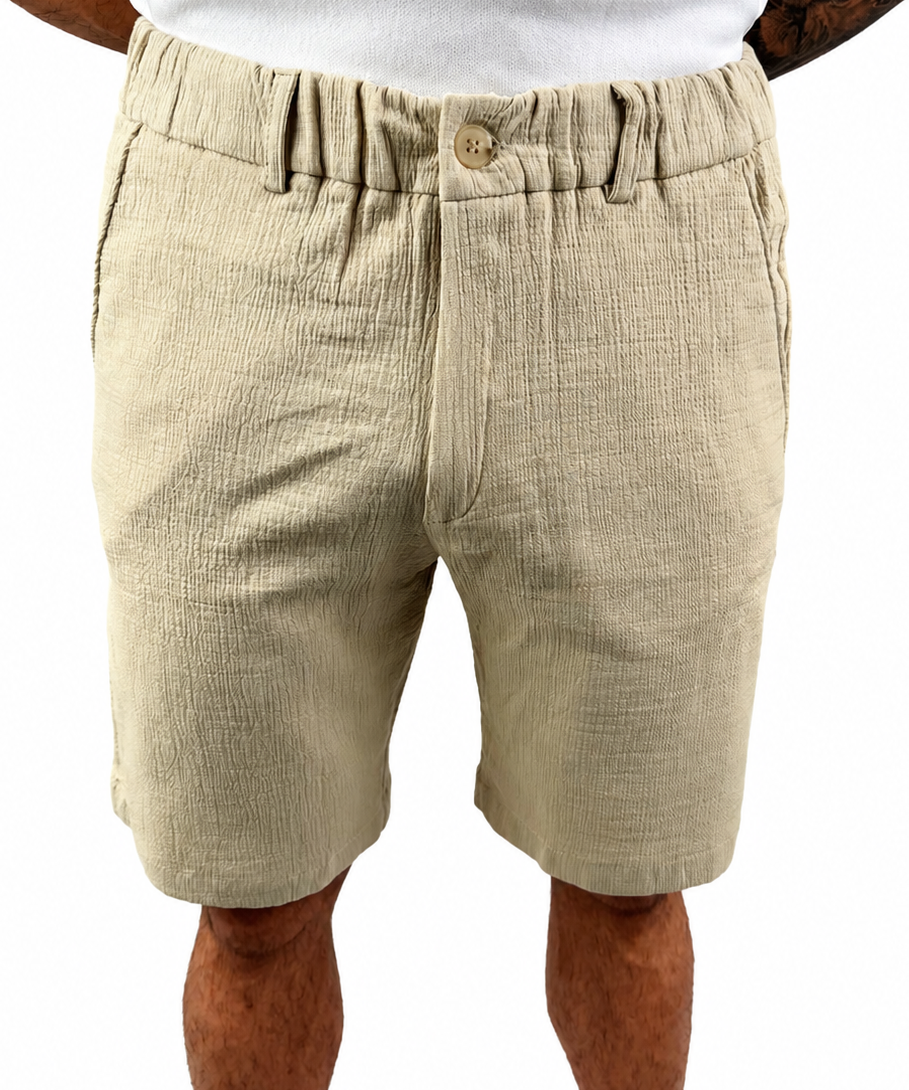 A man wearing beige textured linen shorts with an elastic waistband and button closure, paired with a white t-shirt, shown from the waist down on a white background.