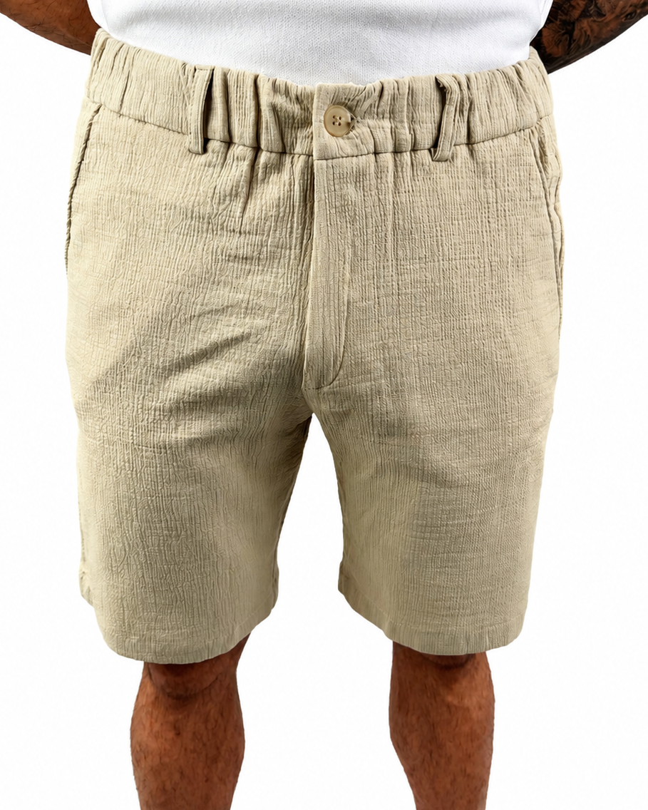 A man wearing beige textured linen shorts with an elastic waistband and button closure, paired with a white t-shirt, shown from the waist down on a white background.