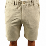 A man wearing beige textured linen shorts with an elastic waistband and button closure, paired with a white t-shirt, shown from the waist down on a white background.