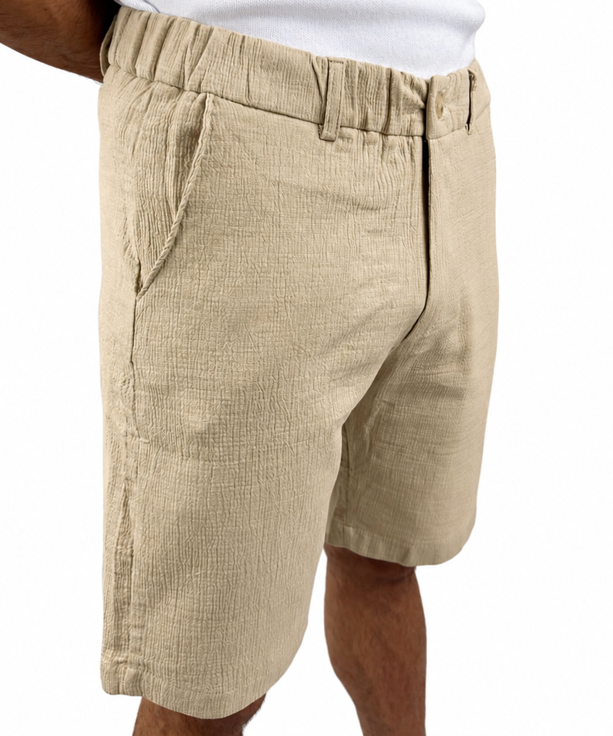 A person wearing beige textured linen shorts and a white tank top, shown from the chest down against a plain white background.