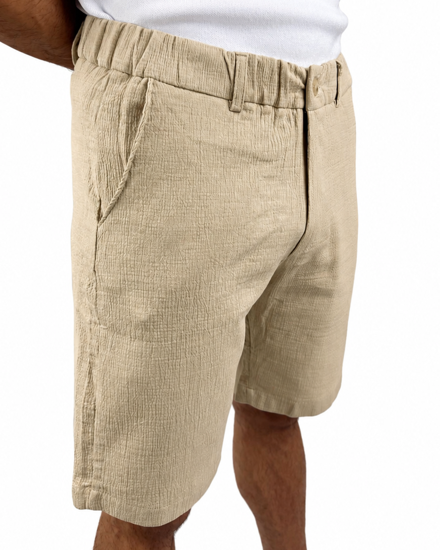 A person wearing beige textured linen shorts and a white tank top, shown from the chest down against a plain white background.