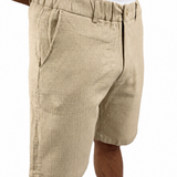 A person wearing beige textured linen shorts and a white tank top, shown from the chest down against a plain white background.