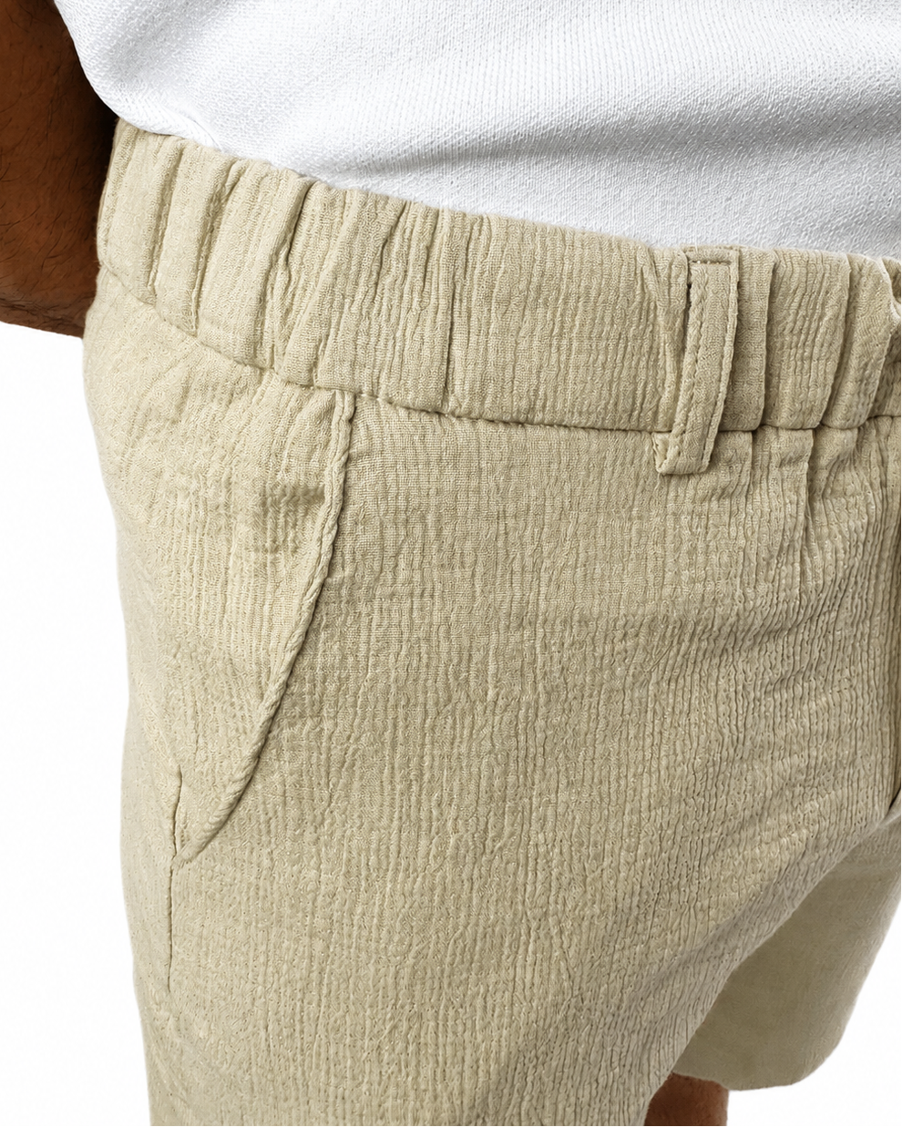 Close-up of a person wearing light beige textured shorts with an elastic waistband and side pockets, paired with a white top against a white background.
