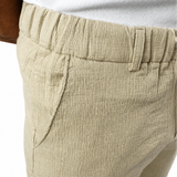 Close-up of a person wearing light beige textured shorts with an elastic waistband and side pockets, paired with a white top against a white background.
